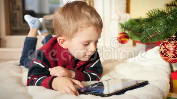 4k视频微笑的小男孩一边躺在地上一边上网一边在平板电脑上玩电子游戏视频的预览图
