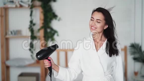穿着白色浴袍的女人用吹风机擦干头发慢动作视频的预览图