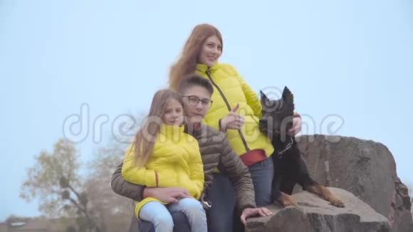 快乐的高加索家庭和他们可爱的狗坐在岩石上哥哥和妹妹和妈妈一起视频的预览图