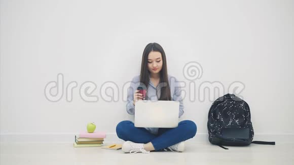 微笑的亚洲女学生坐在洛托斯的位置使用笔记本电脑喝咖啡视频的预览图