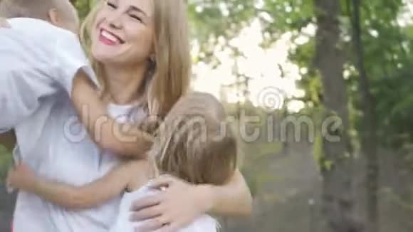 后景可爱的小女孩和男孩拥抱妈妈女人笑着拥抱儿子和女儿公园里的幸福家庭视频的预览图