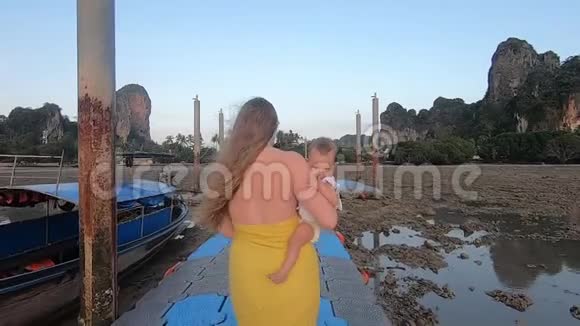 一个穿着黄色衣服的女人抱着一个孩子在一个浮桥码头的高潮黎明时分妈妈和女儿散步视频的预览图