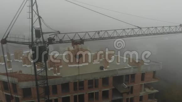 鸟瞰站在居民楼旁雾中的塔吊飞过工地无人机视频的预览图