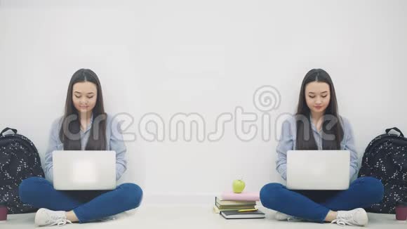 两个可爱的亚洲女孩坐在地板上手拿笔记本电脑点头挥手问好微笑视频的预览图
