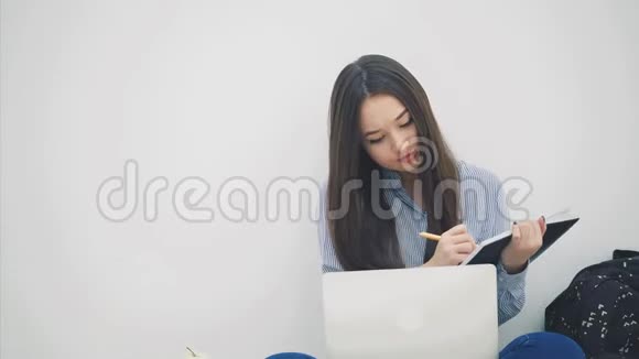 亚洲女士坐在地板上以洛托斯的姿势拿着笔记本电脑把一些东西复制到她的笔记本上视频的预览图
