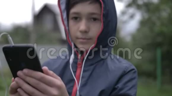 带着耳机的有趣男孩在户外通过电话听音乐视频的预览图