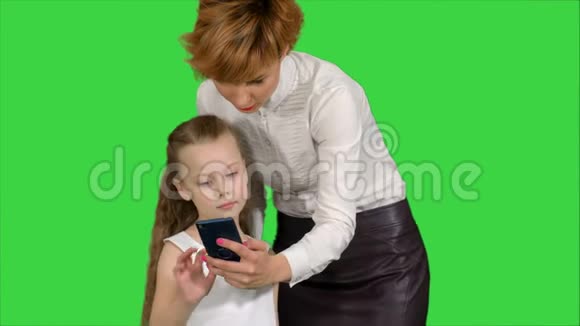 年轻的母亲教女儿如何在绿色屏幕上使用智能手机Chroma键视频的预览图