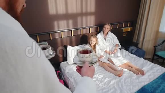 一家人在酒店房间里穿着白色浴袍爸爸把茶杯带到床上视频的预览图