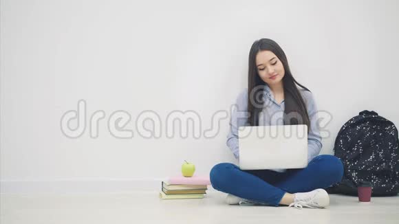 一位亚洲女士坐在地板上拿着笔记本电脑从包里拿出笔和笔记本写字视频的预览图