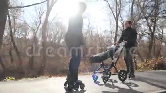 运动的年轻家庭溜冰鞋与婴儿车在温暖的秋天公园妈妈骑着车向后走微笑着视频的预览图