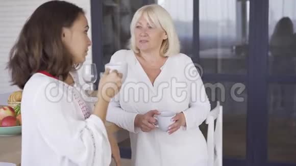 年轻的女人和她的母亲喝茶或咖啡聊天两个女人分享她们的秘密和问题友好视频的预览图