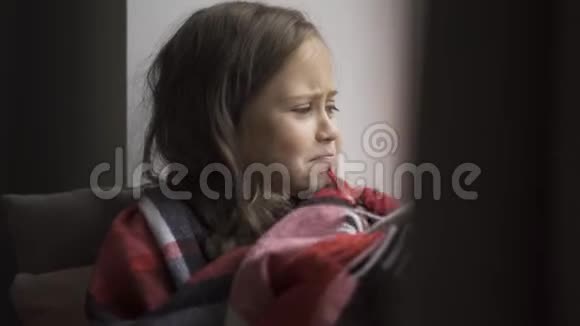可爱的白种人孩子被温暖的毯子覆盖在窗台上坐在家里咳嗽一个棕色头发的女孩视频的预览图