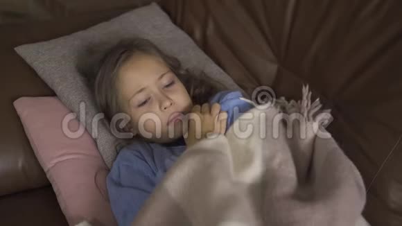 年轻的白种人女孩穿着蓝色毛衣躺在温暖的毯子下温度小病的特写视频的预览图