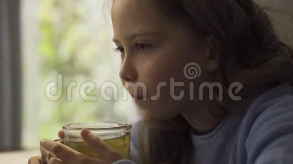 一个可爱的灰眼小女孩的特写桌前端着一杯热茶白种人儿童享受热饮视频的预览图