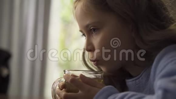 一个留着长长卷发的小白种人女孩的特写吹在一杯洋甘菊茶上可爱的深黑肤色的孩子视频的预览图