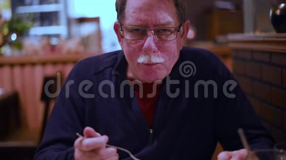 英俊的老人坐在餐馆里咀嚼食物看镜头视频的预览图