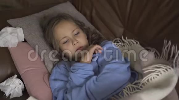 生病的年轻女孩在家里躺在毯子下面用温度计测量体温孩子发烧了视频的预览图