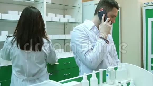 年轻的男性药剂师在药房检查处方时用手机交谈视频的预览图