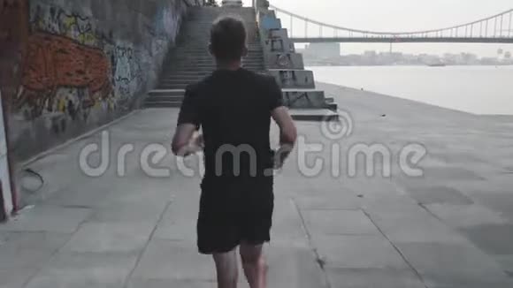 苗条健康运动员在码头跑步的后视镜活泼好动的人沿着河跑小男孩在附近的长廊上奔跑视频的预览图