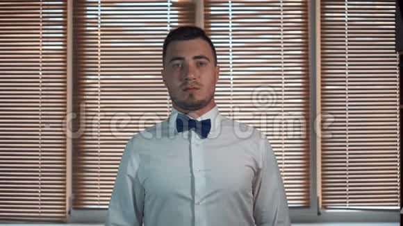 一个穿着白色衬衫带着一张严肃脸的蝴蝶结的年轻人开始微笑一位时尚男士的时尚肖像视频的预览图