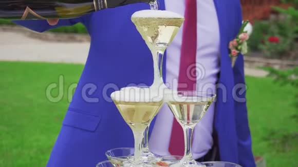 一个穿着蓝色西装的男人把香槟倒进站在金字塔里的玻璃杯里视频的预览图