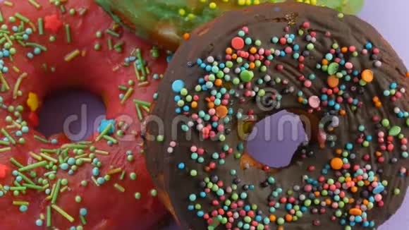美国甜甜圈五颜六色的釉和粉末在紫色背景上旋转近景视频的预览图