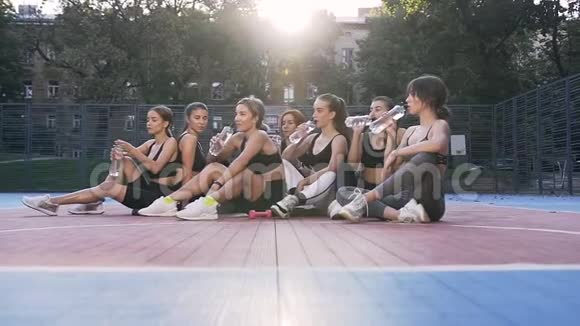 有吸引力的健身女队在户外体育场地板上放松运动后喝水视频的预览图