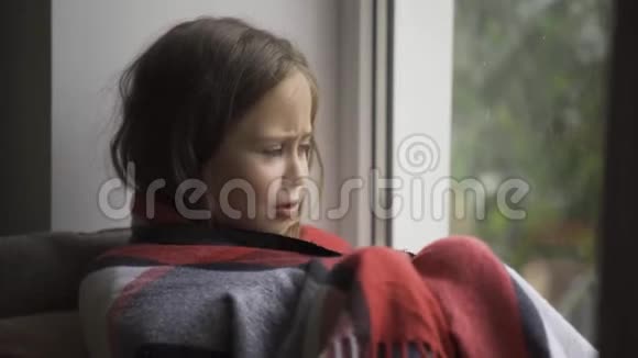 一个深褐色头发的女孩的特写镜头她被温暖的毯子覆盖在家里的窗台上白种人发烧儿童视频的预览图
