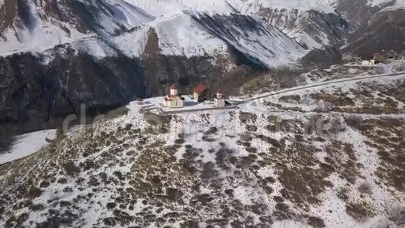 在山上的一座教堂上空盘旋俯瞰着一座雪山峡谷视频的预览图