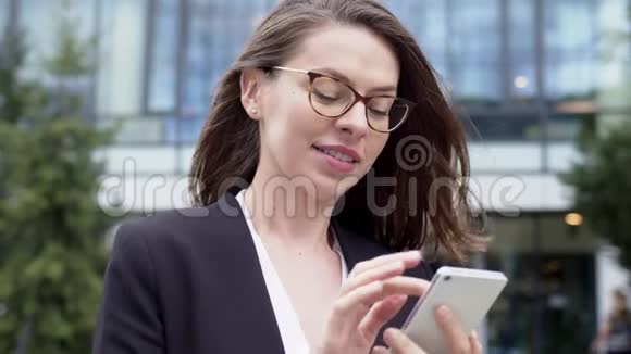 大风天女企业家在办公楼附近的智能手机上讲话视频的预览图