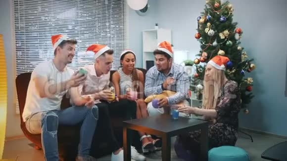 圣诞老人帽子上的快乐朋友在圣诞派对上用智能手机打视频电话视频的预览图