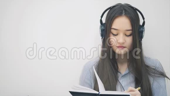 充满灵感的年轻亚洲女孩坐在地板上戴着耳机听着音乐写作切换歌曲视频的预览图