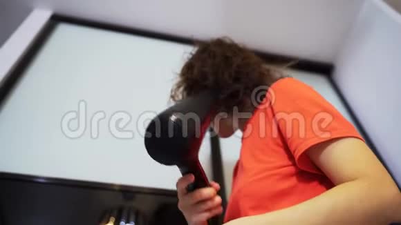 一个穿红色T恤的女人用吹风机擦干头发视频的预览图