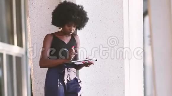 年轻的黑人女孩写在笔记本上站在市中心户外视频的预览图