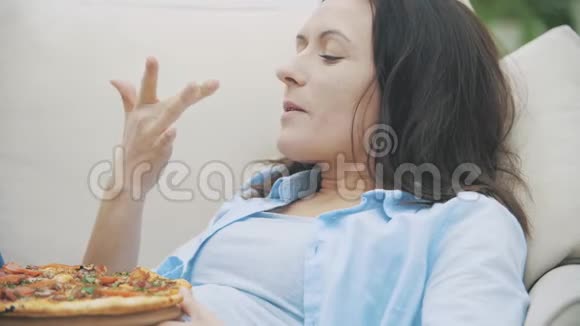 慢点一个年轻的女人正在舔她的手指一边看电视一边吃披萨4K视频的预览图