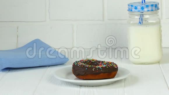 在一罐牛奶和一罐蓝色的砖墙旁边白色盘子上有彩色粉末的大巧克力甜甜圈视频的预览图
