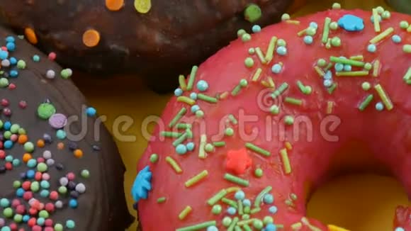 美国甜甜圈五颜六色的釉和粉末在黄色背景上旋转近距离观看视频的预览图