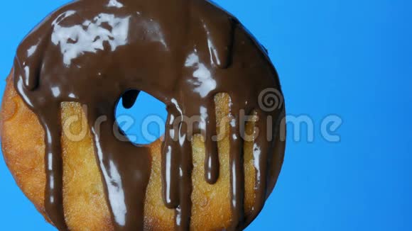 叉子上的圆形大甜甜圈上面有巧克力糖霜和蓝色粉末在蓝色的背景上旋转视频的预览图