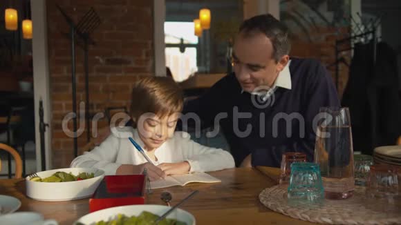 父亲和儿子在咖啡馆里男孩在笔记本上写字视频的预览图