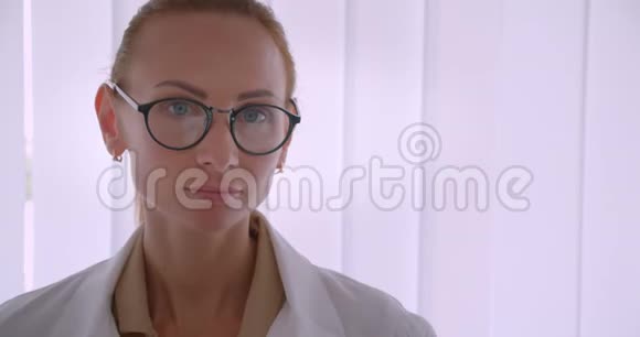 穿着白大褂的职业白种人女医生在医院里修眼镜平静地微笑着进入镜头视频的预览图