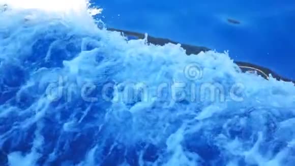 从摩托艇侧面观看游泳和溅起清澈的海水帆船漂浮并在海面上留下痕迹视频的预览图