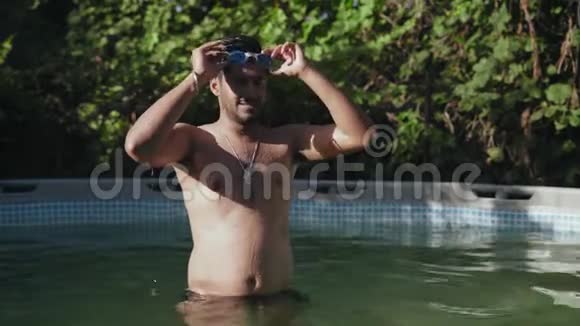 穿着护目镜在浅水池游泳和潜水的印度男人然后用他的脸擦视频的预览图