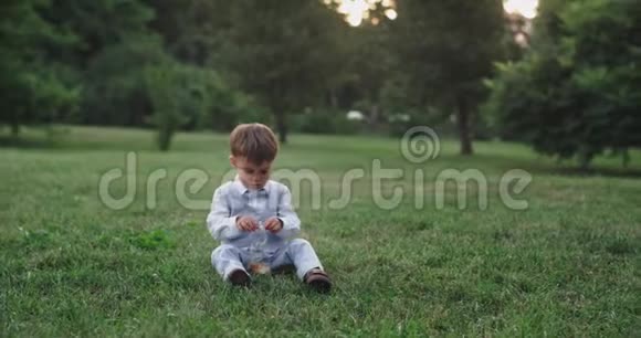 可爱的小男孩穿着休闲服吃着放松的零食在草地上享受公园里的时光视频的预览图