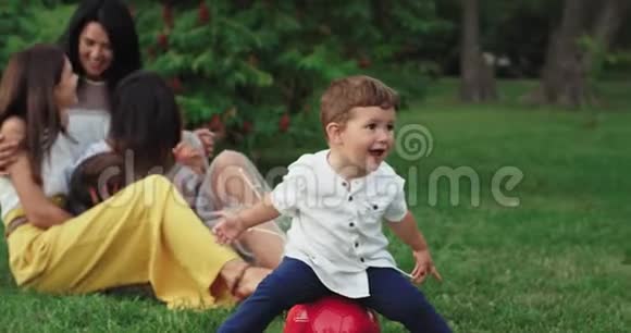 有趣的小男孩坐在红球背景上他的大家庭在公园中央度过了一段美好的时光视频的预览图