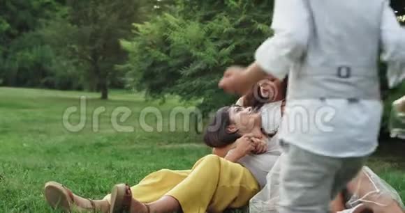 两个有魅力的女士和一个可爱的小男孩躺在草地上微笑着享受在一起的时光视频的预览图