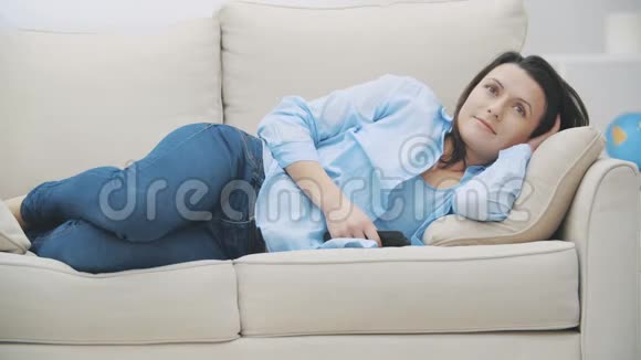 满意的黑发女人正在看电视在家里的沙发上睡着了女人正在做着令人愉快的梦4K视频的预览图