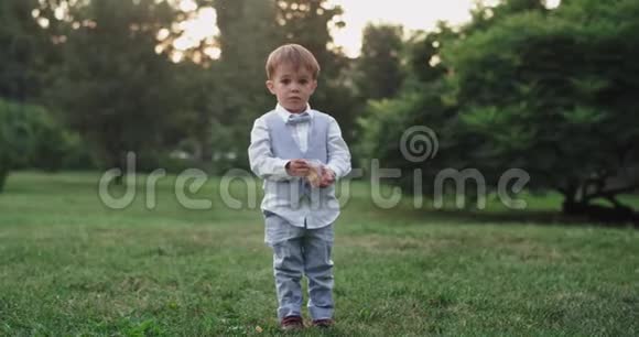 可爱的小男孩穿着一件绿色的衣服在中央公园的一块绿色的田野里在镜头前吃着零食视频的预览图