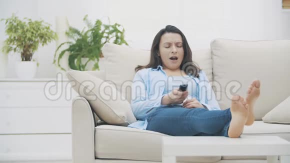 漂亮的女人看电视打哈欠坐在家里的沙发上感到无聊突然她尖叫着她的兴奋视频的预览图