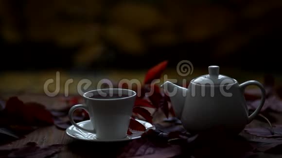 桌子上是热茶和茶壶蒸汽来自一个杯子桌子上摆着一副野葡萄秋叶的装饰秋天视频的预览图