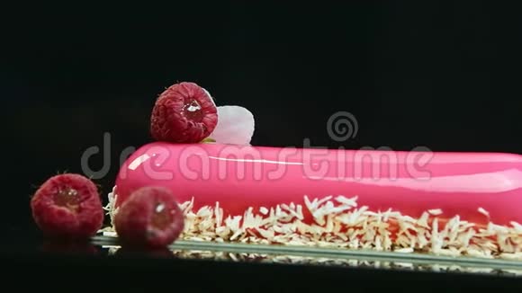 在粉红色釉面长椭圆形蛋糕与椰子刨花和覆盆子的特写全景视频的预览图